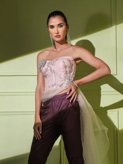 This look pairs a delicate blush pink corset, featuring intricate silver embroidery and a sheer tulle trail, with tailored trousers. It's a modern, powerful take on evening wear.