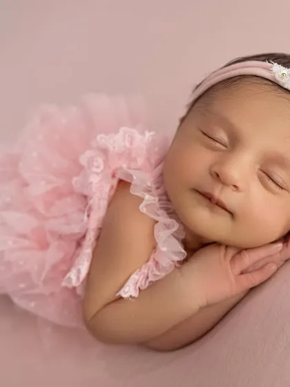 A close up of the baby in the pink dress, capturing a gentle, sleepy smile. The soft lighting enhances her peaceful expression.