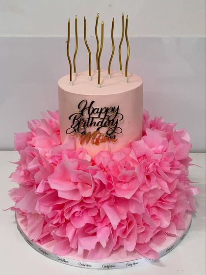 A still image of the beautiful last-minute pink ruffle cake, topped with a "Happy Birthday Mom" charm and elegant gold candles.
