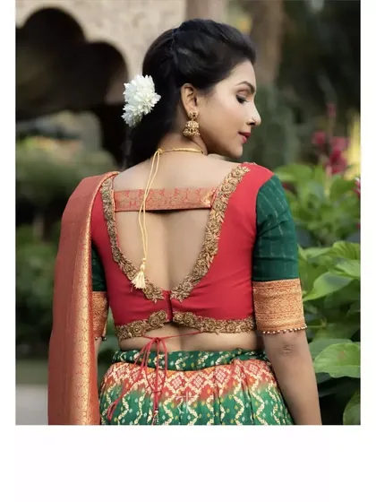 The back view of the red and green blouse, showing its elegant cut and the delicate tassel detail. It pairs beautifully with the traditional drape of the skirt.