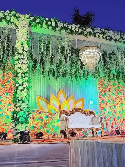 The same colorful floral stage seen from a different angle, highlighting the hanging chandeliers and the lush greenery.