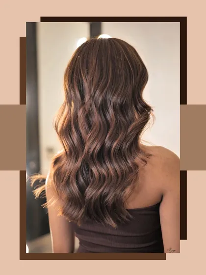 A beautiful shot of a client's fresh balayage, showcasing the rich chocolate and caramel tones styled into perfect waves. This is our signature Iconic Browns look.