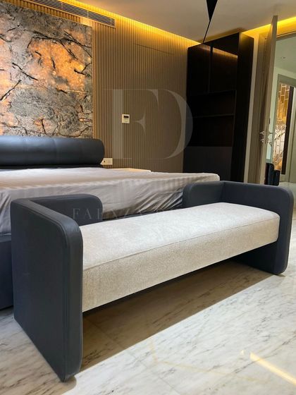 A custom-designed bench for the foot of the bed. The piece features a two-tone design, combining a light fabric seat with a dark leather frame, perfectly matching the room's bed and headboard.