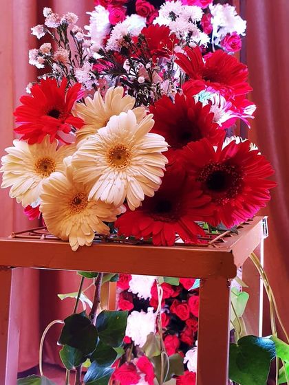A rustic floral arrangement featuring bright red and white gerbera daisies on a wooden pedestal. This style is perfect for adding a pop of color to a reception or engagement party.