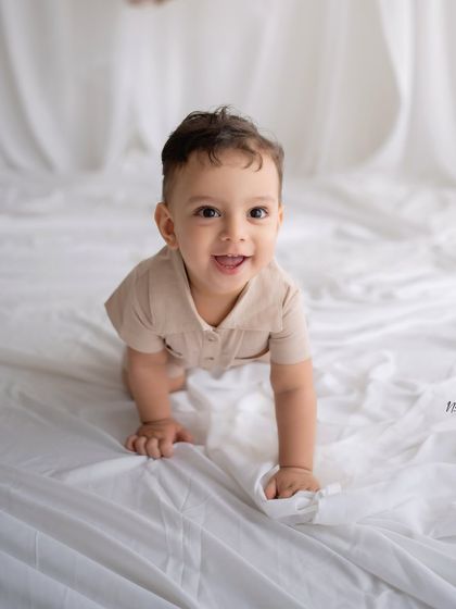 A happy baby crawling on a white sheet, looking right at the camera.