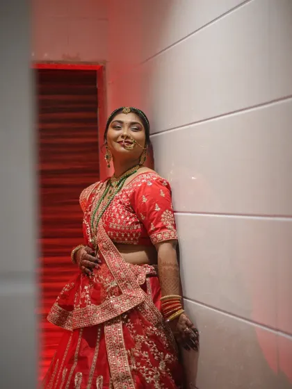 A full-length bridal portrait with dramatic red lighting. This shot captures the bride's confident pose and the stunning details of her red lehenga.