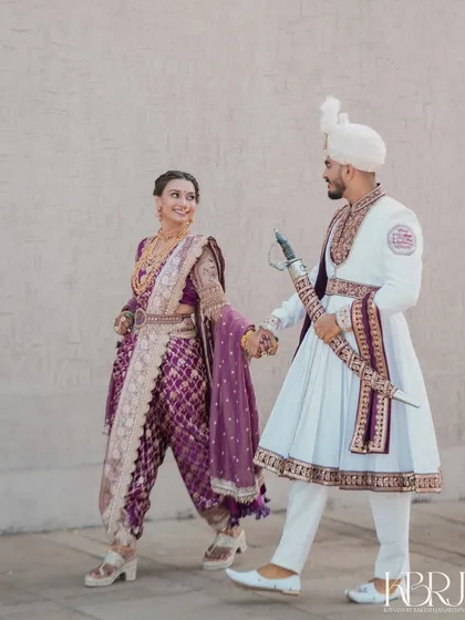 A playful and happy moment. The bride leads the groom, both smiling, dressed in their beautiful Maharashtrian wedding attire.