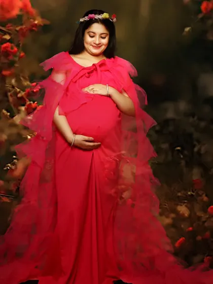 A dreamy solo maternity portrait of a woman in a red gown, standing in an enchanted forest setting.