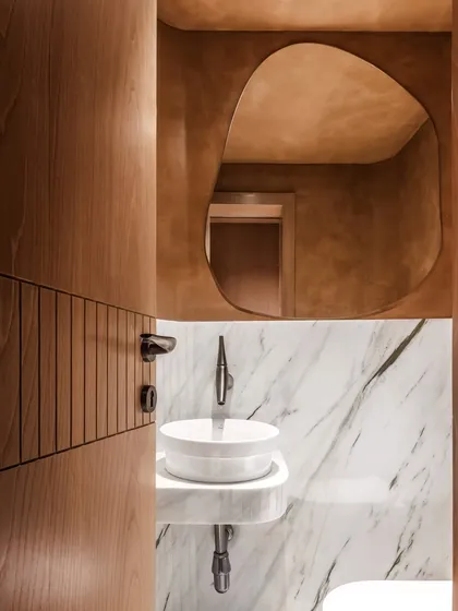 The powder room is a harmony of elegance, where Calacutta gold marble meets a rustic oak veneered door. The walls are finished with an earthy-toned texture paint, and an organic-shaped mirror adds a soft, sophisticated touch.