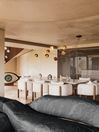 A wider view of the dining and living areas, showcasing the open-concept layout. The sculptural sofa in the foreground frames the scene, leading the eye towards the dining table and the art beyond.