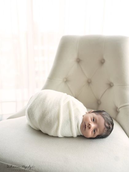 Simple, pure, and peaceful. A newborn wrapped in a soft white blanket, resting on an elegant chair, creates a timeless and classic image.