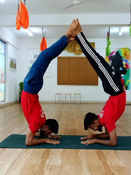 Two students form a house shape with their bodies in a partner forearm stand. This is a testament to their shared strength, balance, and coordination.