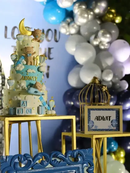 A detailed shot of the beautiful themed cake next to the shimmering backdrop. The setup on gold pedestal tables adds a touch of elegance to the first birthday celebration.