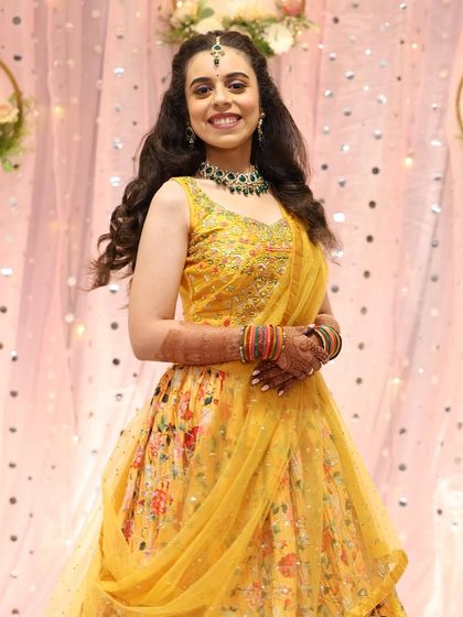 A full-length shot of the bride's cheerful sangeet outfit. The hairstyle is kept soft with curls to match the playful vibe.