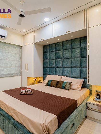 This cozy master bedroom features a beautiful tufted teal headboard set against the wall, with full-height wardrobes providing ample storage. The design is clean, modern, and incredibly restful.