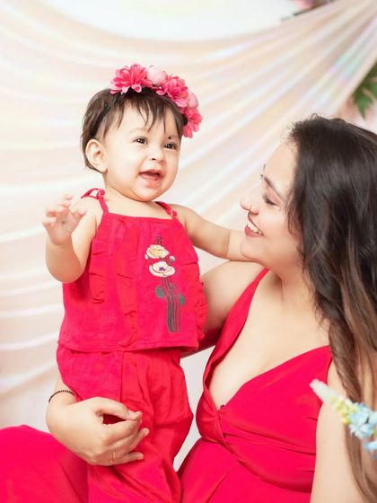 A mother and her smiling baby girl, both dressed in red for a vibrant and joyful portrait.