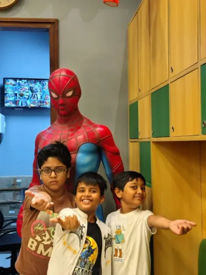 Three young fans strike a pose with a life-sized Spiderman statue, ready for a web-slinging adventure.