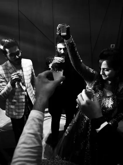 A black and white photo capturing the party atmosphere, with guests raising their glasses for a toast.