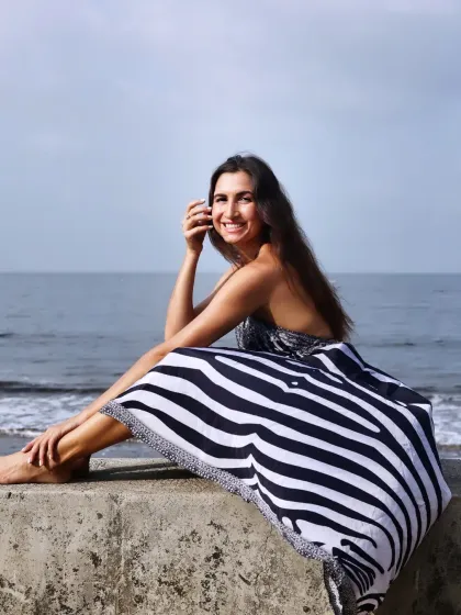 A happy and relaxed portrait of a model sitting on a sea wall, smiling at the camera.