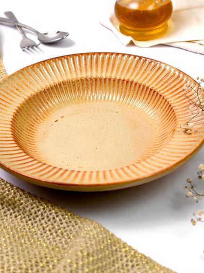 This textured ceramic pasta bowl is styled with a rustic jute cloth and delicate baby's breath. The bright, clean lighting highlights the intricate lines and warm, earthy tones of the plate.