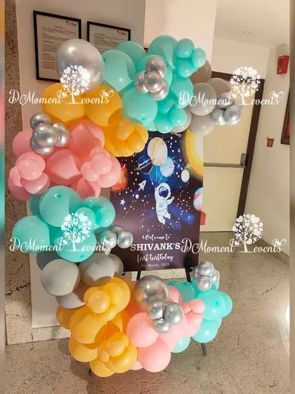 A welcome sign for Shivank's space-themed party, featuring a beautiful galaxy print and framed by a creative arrangement of orange, teal, and silver balloons.