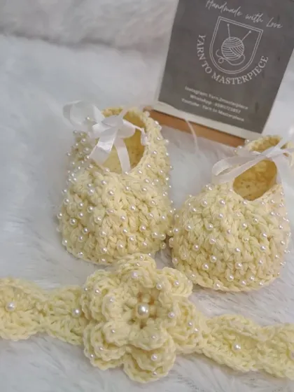 A beautiful and delicate set in a pale yellow, this includes pearl-studded booties and a matching headband with a pearl-centered flower.