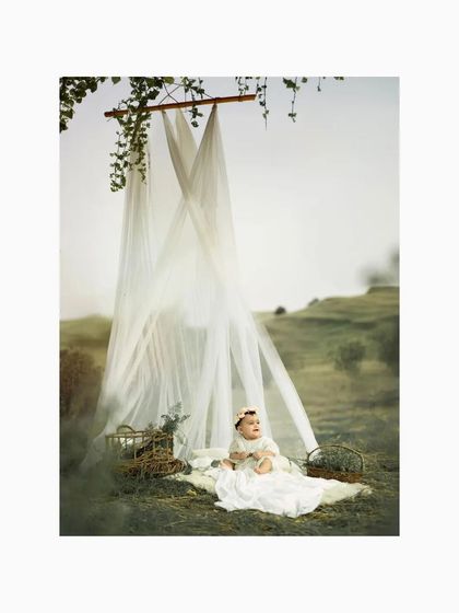 The baby sits up and looks around, her curiosity sparked by the beautiful outdoor setting. The soft, diffused light and natural surroundings make for a truly angelic portrait.
