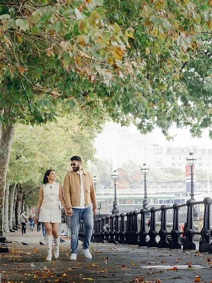 A romantic walk under the autumn trees in London. Their coordinated beige and white outfits create a soft, harmonious look that is perfect for a daytime stroll.