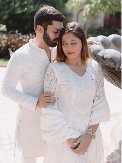 A tender pre-wedding portrait, with the couple dressed in elegant white, sharing a quiet embrace near a garden fountain.