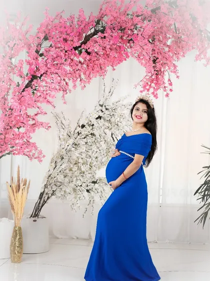 A beautiful portrait set against a wall of pink cherry blossoms. The royal blue gown provides a striking color contrast, making the expecting mother stand out.