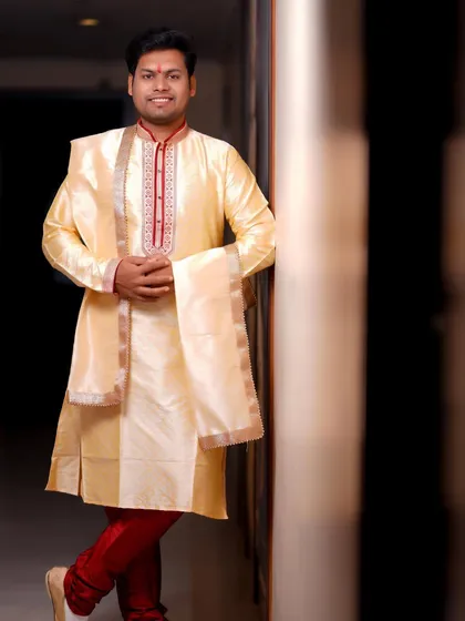 A handsome portrait of the groom. He leans against a wall, smiling, his cream-colored kurta and red trousers making for a classic and stylish look.