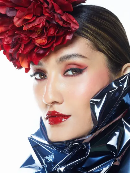 A classic and bold look featuring a vibrant red lip, subtle winged liner, and a statement red floral headpiece.