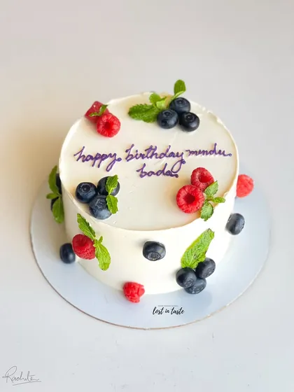 A simple yet beautiful celebration cake with chocolate buttercream, decorated with fresh raspberries, blueberries, and mint leaves for a pop of color and flavor.