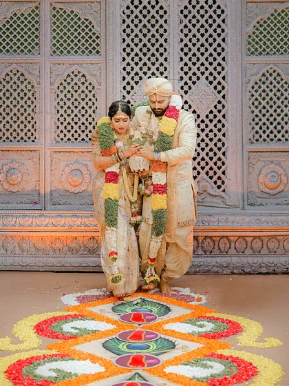 The couple participates in a wedding ritual. This photo provides a clear view of the groom's complete outfit, including the silk dhoti and the way the embroidered shawl is draped.