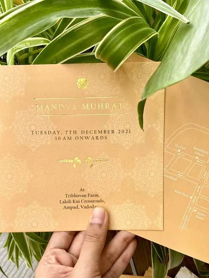 A card for the 'Mandva Muhurat' ceremony, featuring delicate mandala patterns and gold foil details. The design includes a simple map on the back for guests' convenience.