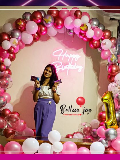 A happy client enjoying her stylish birthday setup. This circular balloon arch in shades of pink and silver, complete with a neon sign, provides the perfect backdrop for birthday photos.