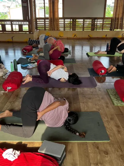 A class of students in a gentle twisting pose, using the support of the floor to release tension in the back.