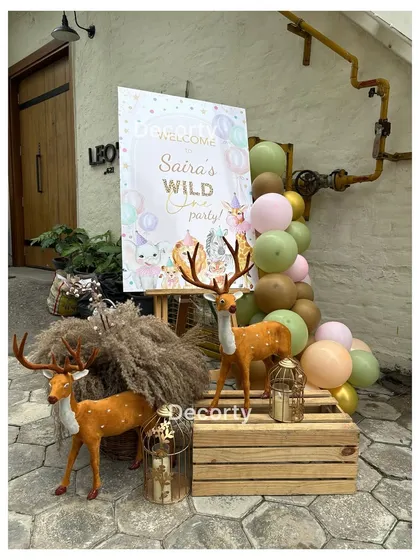 A rustic welcome sign for Saira's "Wild One" party, decorated with pampas grass, deer props, and pastel balloons.
