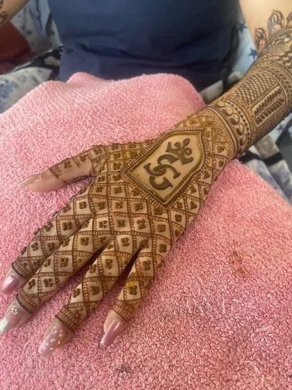 A close-up of a personalized initial 'SG' inside an arched frame, surrounded by a classic 'jaali' or net pattern on the back of the hand.