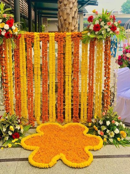 A simple yet beautiful Haldi photo corner. This setup features a backdrop of hanging orange and yellow marigold garlands, perfect for capturing memories.