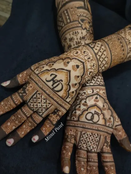 A close-up of an engagement mehndi, showing the couple's initials "KD" and interlocking rings, framed by beautiful arches.