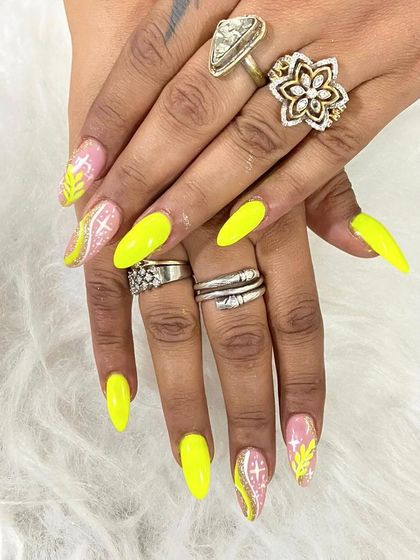 A bright and bold set of neon yellow extensions with glitter and leaf-patterned accent nails.