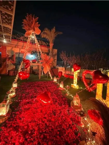 A breathtaking outdoor proposal or romantic dinner setup. A path of red rose petals and lanterns leads to a beautifully decorated canopy tent under the stars.