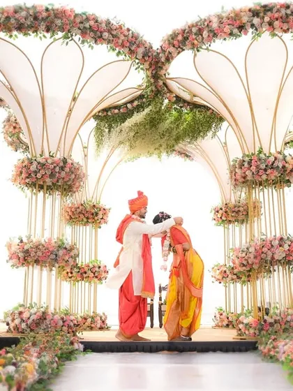 A breathtaking wide shot of a Maharashtrian wedding ceremony under a magnificent floral mandap by the sea.
