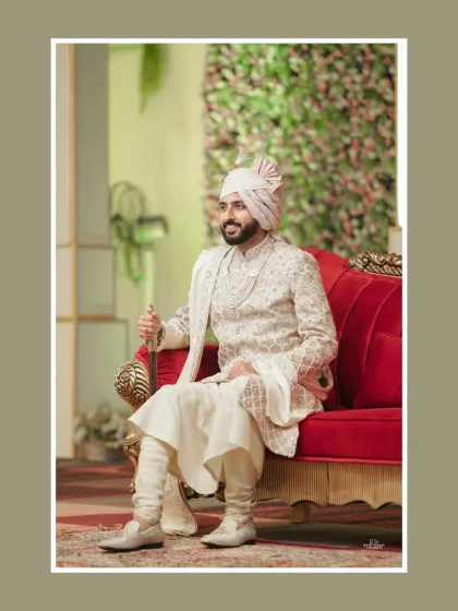 The groom seated majestically on a red sofa, holding his ceremonial sword. A portrait 금액 royalty and tradition.