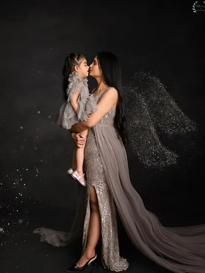 An aspirational and artistic portrait of a mother and daughter. The mother, in an elegant gown with sparkling angel wings, holds her daughter close, creating a magical and emotionally powerful image of their bond.