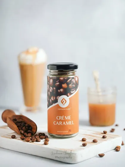 A bright and airy shot of Crème Caramel flavored coffee. The focus is on the product jar, with a beautifully prepared coffee drink blurred in the background to suggest the end result.