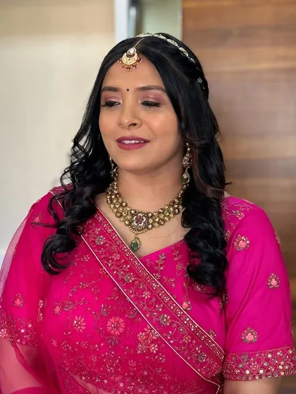 This client is ready for a wedding in her bright pink outfit. The makeup features a soft smokey eye and a maang tikka for a traditional touch.