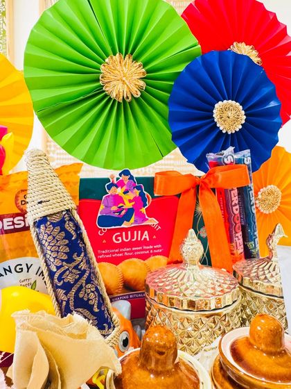 A close-up of the traditional Holi hamper, showcasing the exquisite details. You can see the ornate glass jars, a brocade-wrapped pichkari, and a box of Gujia, blending festive elegance with timeless traditions.