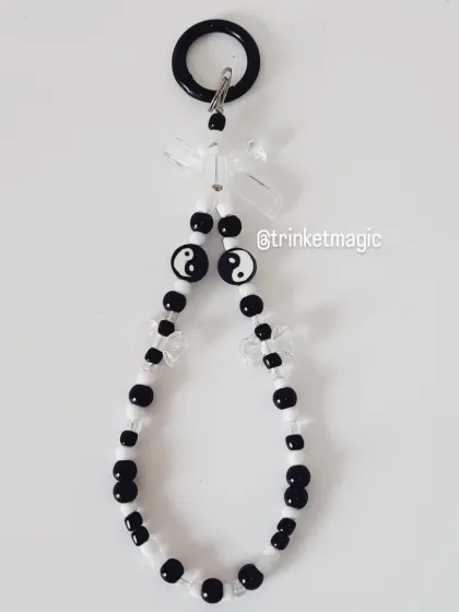 This phone charm features a balanced mix of black and white beads with yin-yang symbols and clear bows.